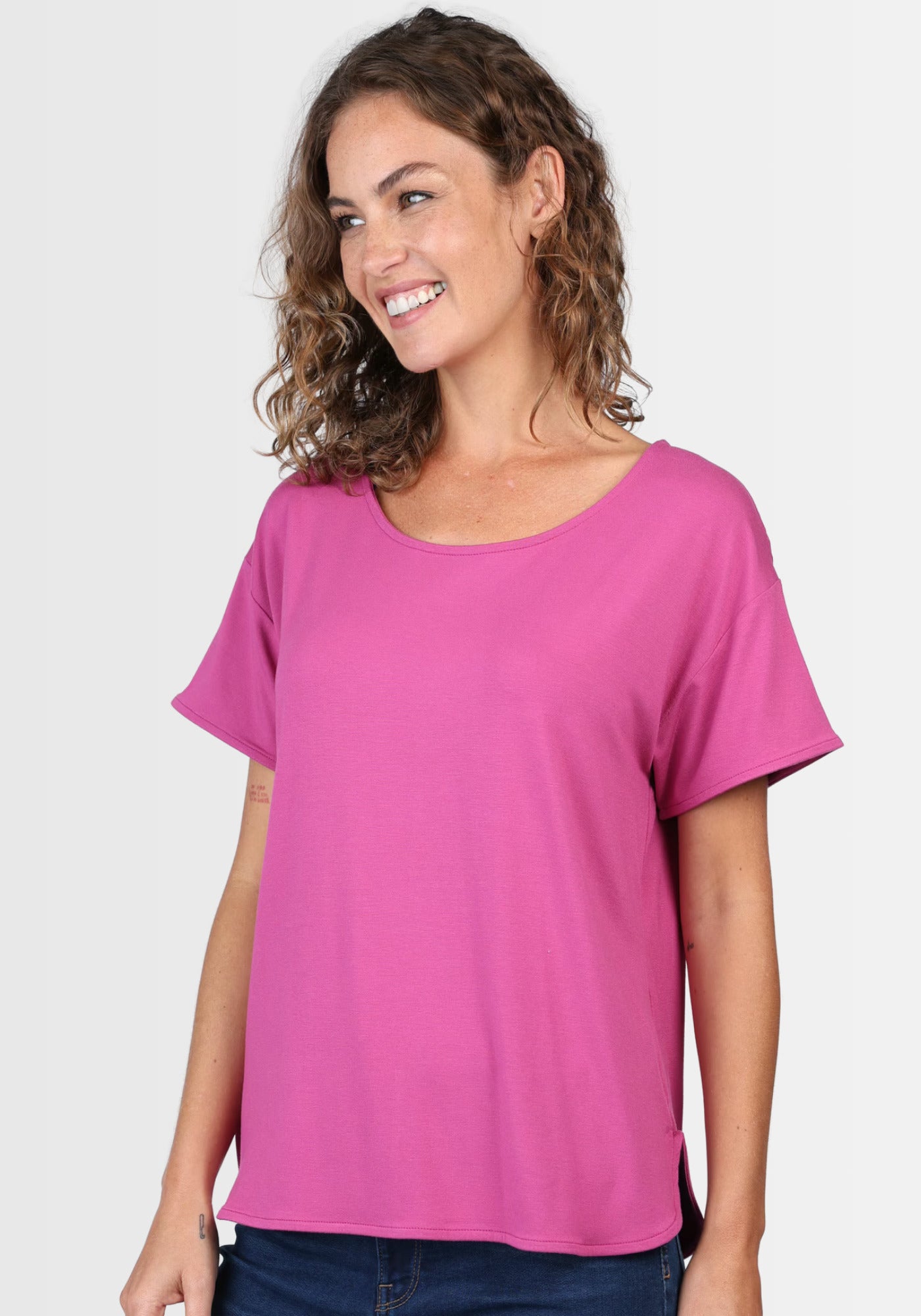 Frau lächelt in die Kamera und präsentiert das T-Shirt „Betzi“ in Raspberry, das dank seiner elastischen Viskosequalität jede Bewegung mitmacht.