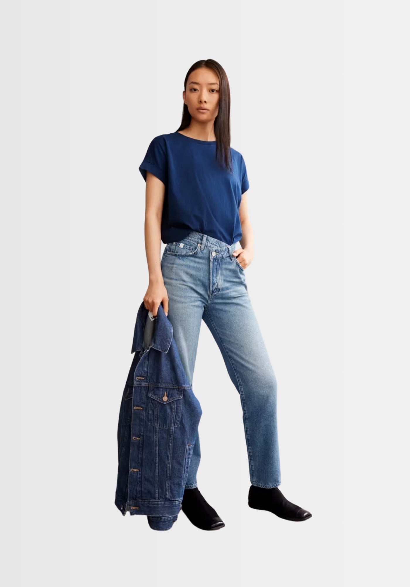 Model trägt das locker geschnittene IDAARA T-Shirt in Faded Indigo, kombiniert mit einer hellen Jeans und passender Denim-Jacke in der Hand.