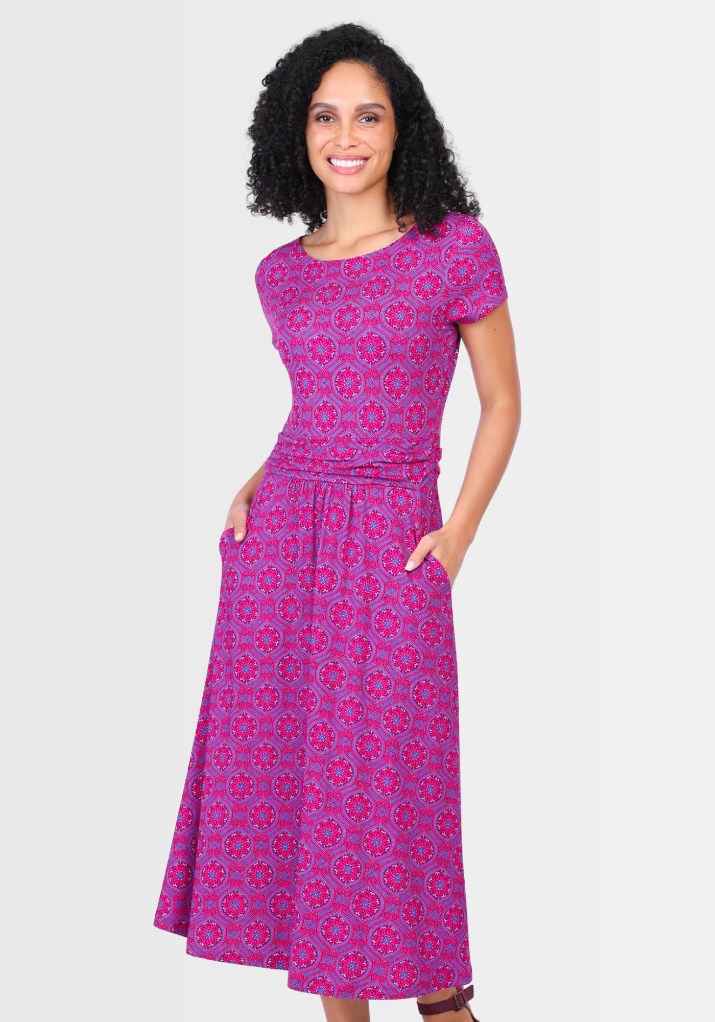 Seitenansicht des taillierten Midikleids „Malind mandala“ in Himbeerrot. Die lässigen Eingrifftaschen und die charmante Raffung im Rock sorgen für eine schmeichelhafte Silhouette, ideal für warme Tage.