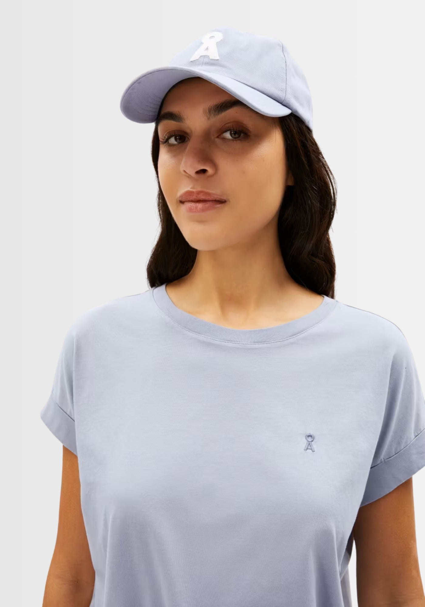 Model trägt das Idaara T-Shirt in zartem Graublau (Misty Morning) mit aufgenähter Logostickerei auf der Brust und passender Cap, gefertigt aus weicher Bio-Baumwolle.