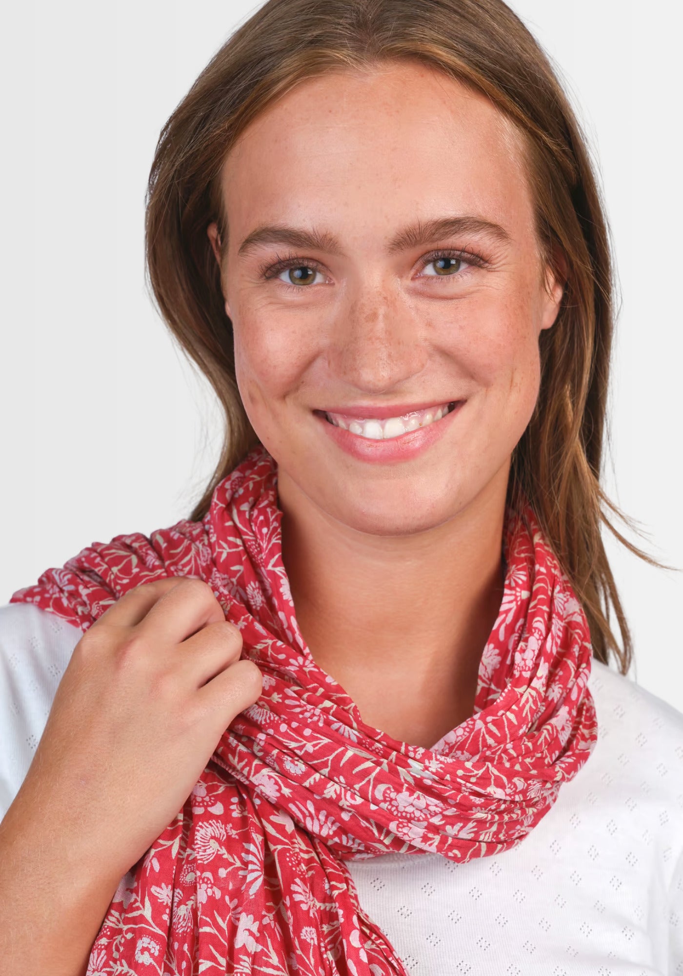 Ein Model präsentiert das Tuch „Lorie – magnolie“ in warmem Rot, das mit seinem romantischen Blumenmuster aus weicher Baumwolle jedem Outfit einen femininen Akzent verleiht.