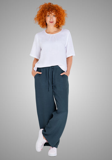 Model trägt eine locker fallende Leinenhose in dunklem Denimblau, kombiniert mit einem weißen Shirt. Die Hose hat eine Seitenlänge von ca. 106 cm in Größe M und bietet dank reinem Leinenmaterial ein luftiges Tragegefühl.