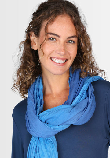 Model trägt das blaue Tuch „Asta“ locker um den Hals, kombiniert mit einer hellen Jeansjacke. Der sanfte Farbverlauf und die softe Baumwollqualität sorgen für ein angenehmes Tragegefühl.