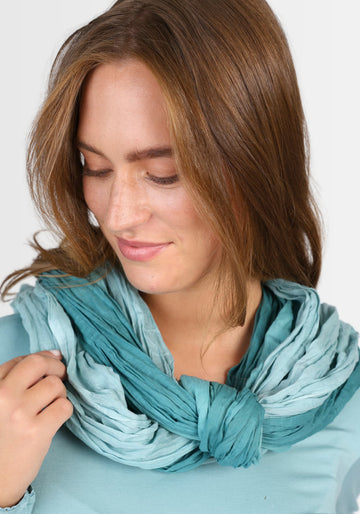 Ein Model präsentiert das Tuch „Asta – Mermaid“ in Blau, das durch seinen einzigartigen, sanften Farbverlauf und die hochwertige Baumwollqualität einen frischen, maritimen Look verleiht – perfekt kombinierbar zu Kleidern und Röcken.

