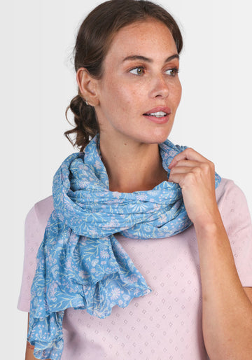 Ein Model trägt das Tuch „Lorie – Swedish Blue“ von Sorgenfri Sylt, das durch sein harmonisches, floral bedrucktes Muster und die angenehme Baumwollqualität einen skandinavisch inspirierten, eleganten Akzent setzt.
